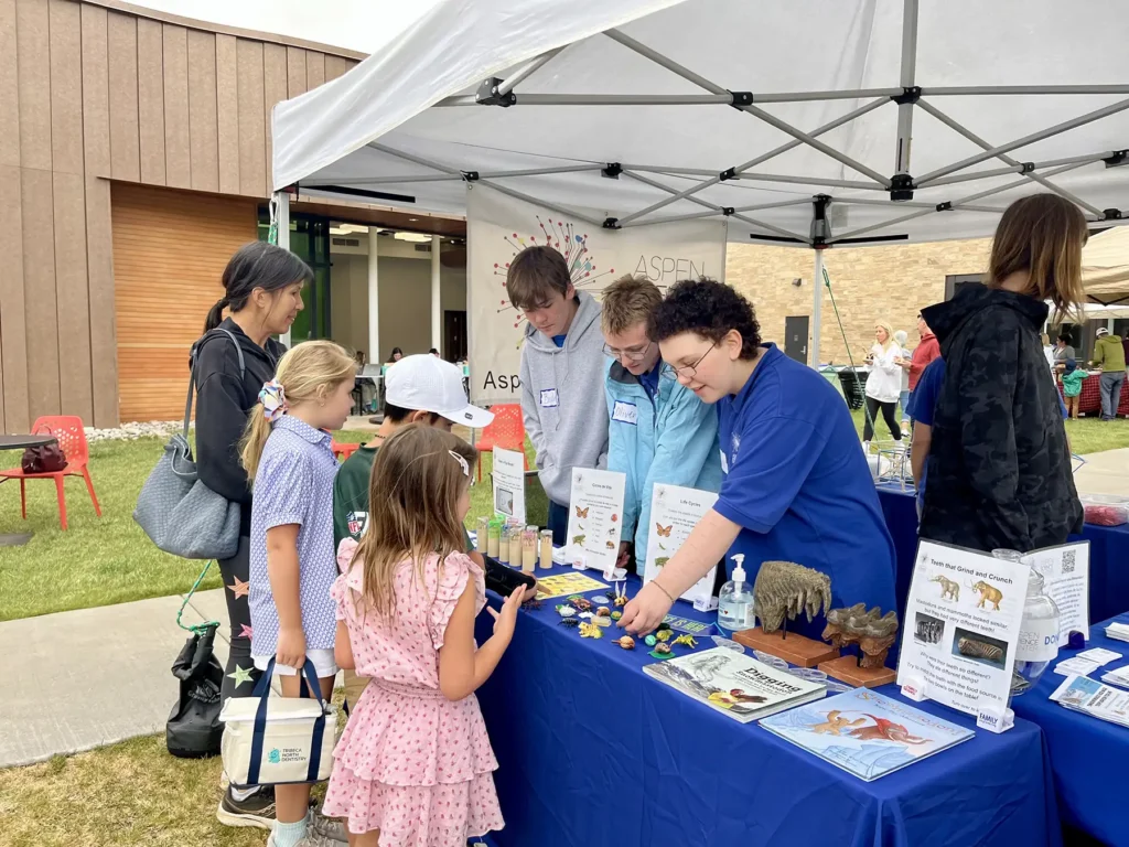 Teenagers stand behind a table at a fair where they teach younger kids about animal biology